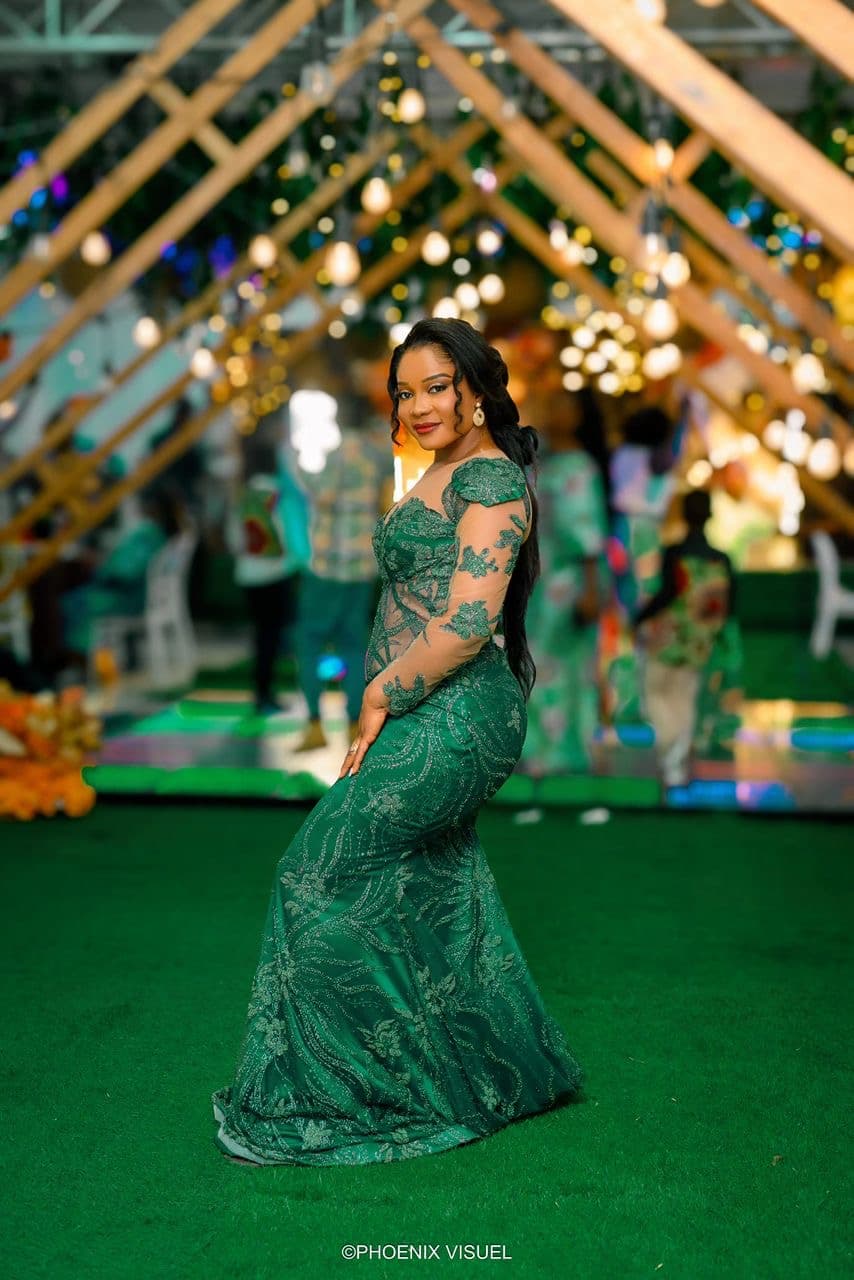 Femme élégante en robe de soirée verte brodée posant dans un décor festif et lumineux.
