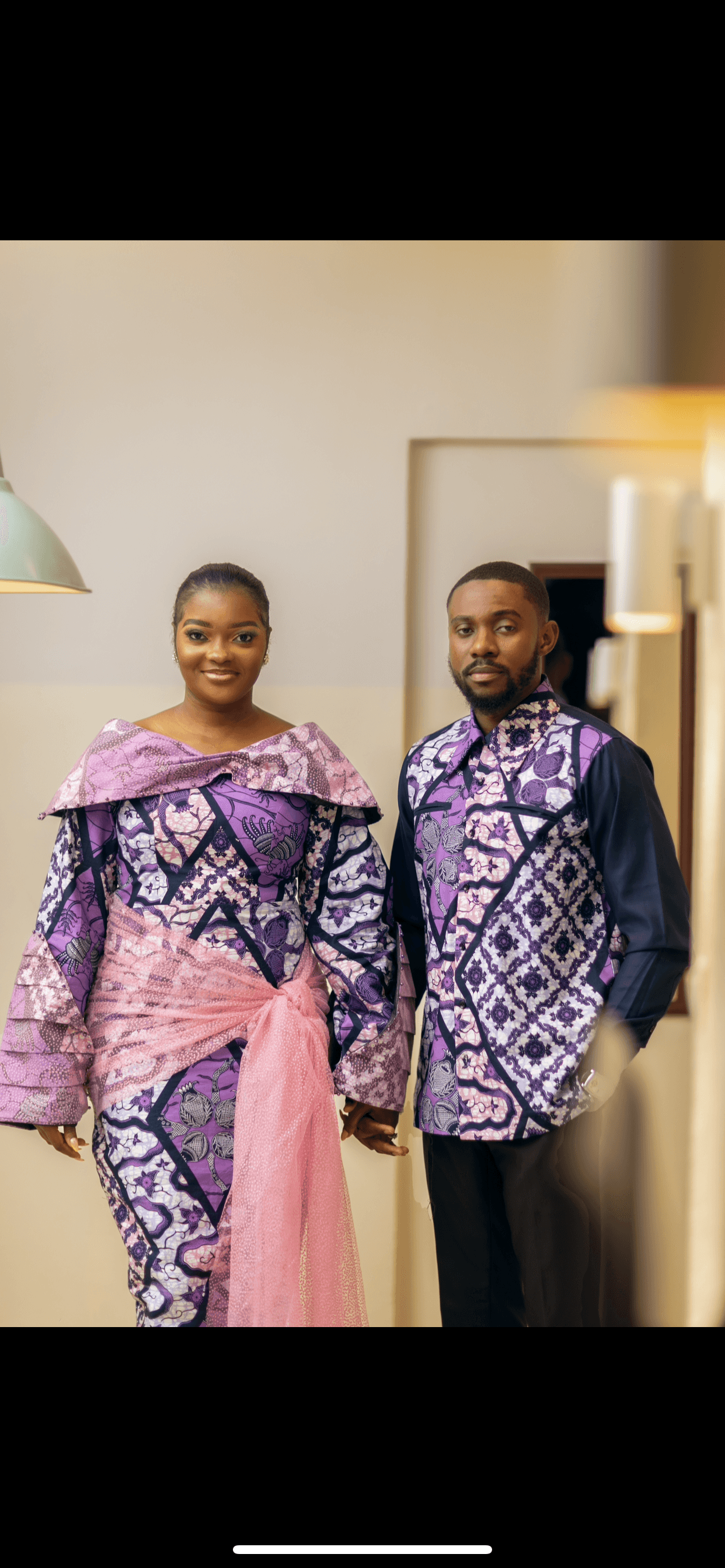 Couple en tenues traditionnelles africaines violettes à motifs assortis se tenant par la main.